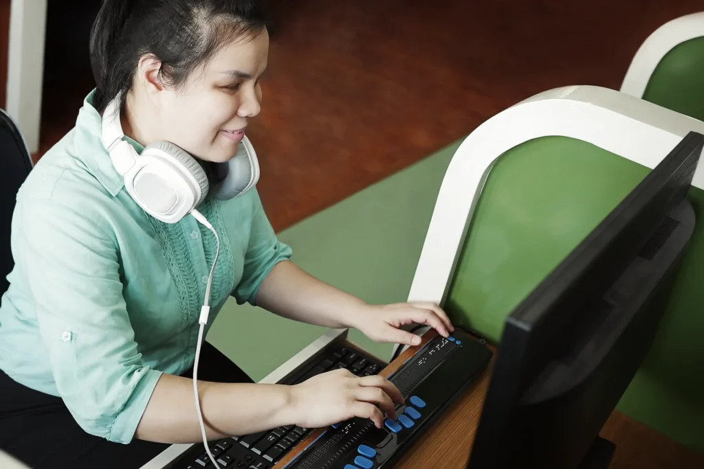 Giovane donna con disabilità visive che utilizza un computer con display braille o terminale braille