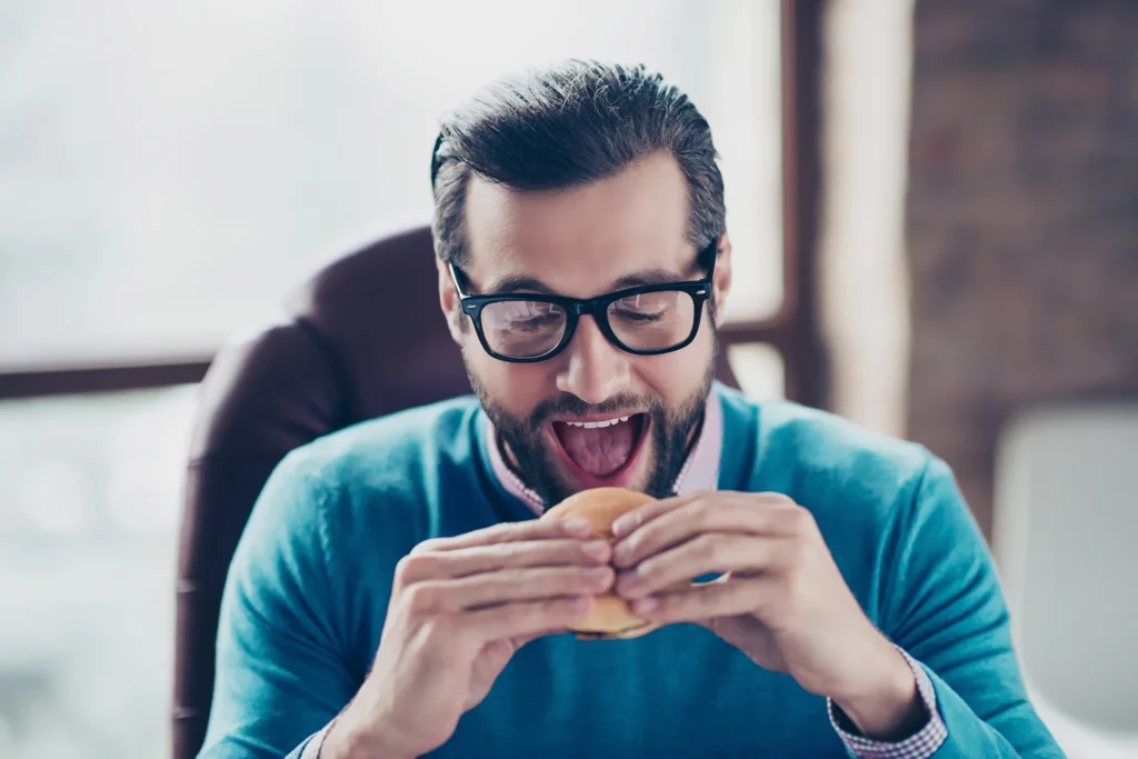 Ritratto ravvicinato di un impegnato affamato che sta per addentare un delizioso cheeseburger tra le mani.